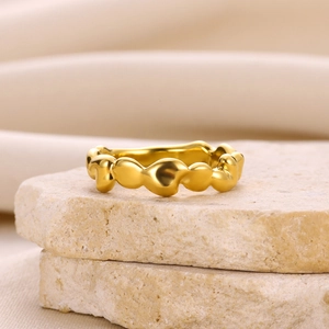 Détail de la bague géométrique dorée avec texture ondulée posée sur des pierres naturelles