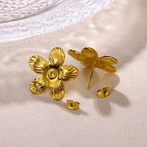Nahaufnahme der goldfarbenen Blumenohrringe mit Textur auf edlem Seidenstoff