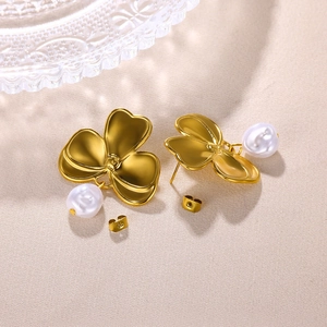Nahaufnahme von 18K Gold Blumenohrringen mit weißen Perlen auf strukturiertem Stoff
