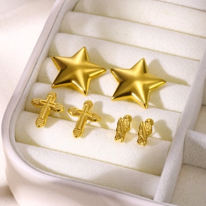 Three pairs of gold stainless steel stud earrings with cross and star patterns on white velvet