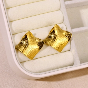 Detailed macro shot of square gold-plated stud earrings with grid texture in a jewelry box
