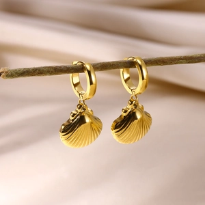 Detailed macro view of golden shell hoop earrings hanging on a natural wooden branch