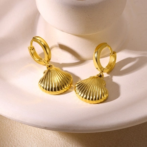 Close-up of golden shell dangle earrings with ribbed texture on a ceramic display