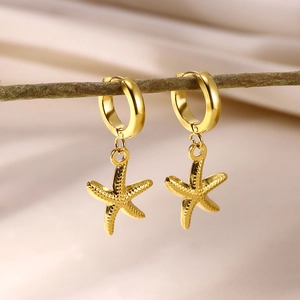 Detail of golden starfish drop earrings on a wooden branch with fabric backdrop