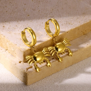 Macro shot of gold crab dangle earrings on beige stone showing refined nautical metalwork