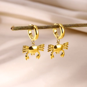 Macro detail of golden crab charm hoop earring on a soft satin and wooden background