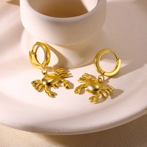 Close-up of golden crab pendant earrings on a minimalist ceramic plate display