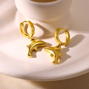 Detail view of golden dolphin pendant earrings with a polished finish on a ceramic stand