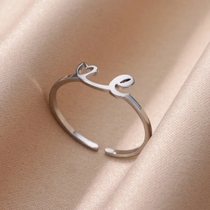 Primer plano de anillo ajustable plateado con corazón y letra E sobre seda suave