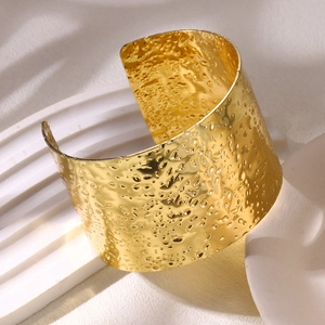 Detailed view of wide gold cuff bracelet featuring a textured hammered metal surface