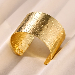 Detail of wide gold hammered cuff bracelet featuring textured water ripple surface
