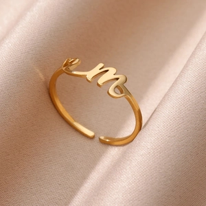 Vista de detalle del anillo ajustable bañado en oro con la letra m sobre fondo raso