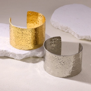 Close-up of gold and silver hammered metal wide cuff bracelets on a stone slab