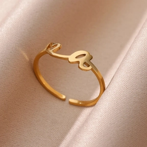 Detalle del anillo ajustable bañado en oro con corazón y letra 'a' sobre seda rosa
