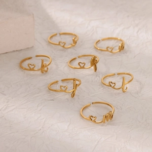 Anillos dorados ajustables con símbolos de corazón y letras sobre un fondo blanco