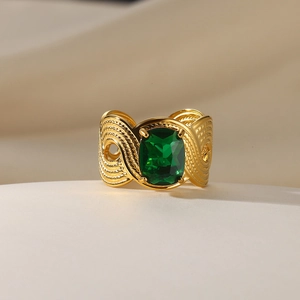 Detailed shot of golden wide band ring with emerald cut green gemstone and woven texture