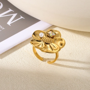 Detail of gold flower ring with pearl and iridescent stone on textured background