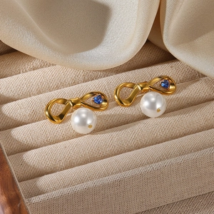 Détail de boucles d'oreilles nœud en or 18K avec zircon cœur bleu et perles blanches