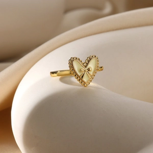 Elegant gold heart ring with cream enamel and bow detail on ceramic display