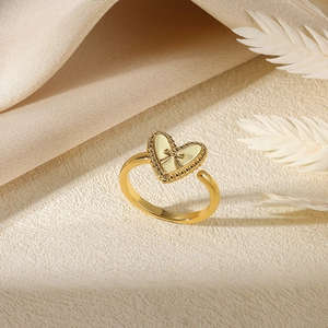 Gold stainless steel open ring with heart pearl and bow detail on a beige silk background
