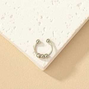 Close-up of silver beaded nose ring with five balls on white textured stone background