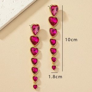 Vista detallada de pendientes largos dorados con cristales rosa en forma de corazón