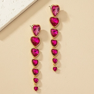 Pendientes largos de oro vintage con piedras de corazón magenta sobre fondo de piedra natural
