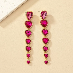 Detalle de pendientes largos dorados con gemas de corazón rosa en cascada de diseño vertical