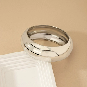 Minimalist silver chunky dome bangle in polished stainless steel on a beige pedestal