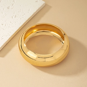 Detailed view of wide polished gold bangle against minimalist stone background