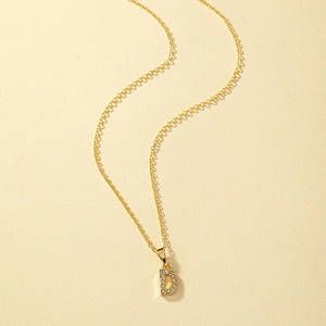 Dettaglio della collana dorata con un pendente scintillante a forma di lettera D maiuscola