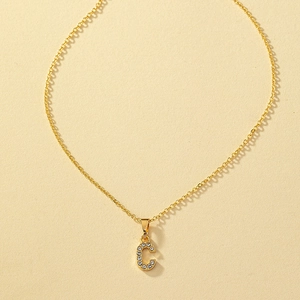 Dettaglio macro della collana dorata con pendente a lettera C e zirconi brillanti