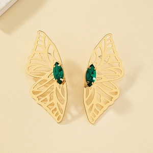 Macro detail of gold hollow butterfly wing earrings with marquise green gemstones