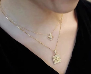 Nahaufnahme der 18K vergoldeten Doppelhalskette mit Fleur-de-Lis- und Zirkon-Anhängern