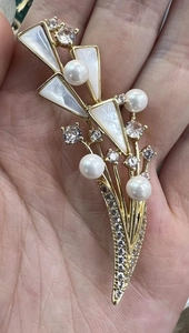 Vue macro d'une broche fleur en or avec pétales en nacre naturelle et perles blanches