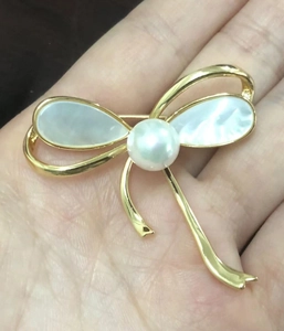 Détail d'une broche noeud dorée avec nacre naturelle et une perle blanche centrale