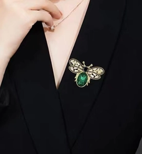 Detailed close-up of a gold honey bee brooch with green zircon on a black blazer