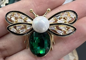 Macro detail of bee brooch featuring green faceted gemstone body and white pearl chest