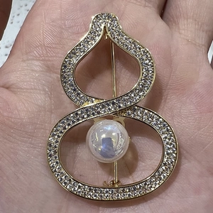 Detailed view of a gold gourd brooch with pavé rhinestones and a large pearl in hand