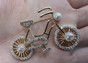 Macro shot of a gold bicycle brooch with rhinestones and pearls held in a hand for size