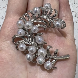 Close-up of silver feather brooch with white pearls held in hand for detail