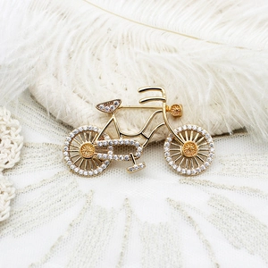 Elegant gold bicycle brooch featuring micro-set green and white zircons on a white feather