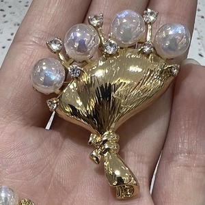 Detailed view of a golden fan-shaped brooch with iridescent pearls and white rhinestones