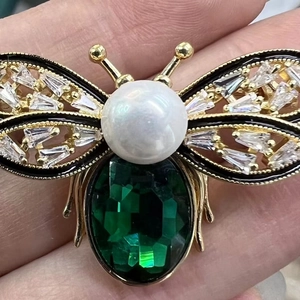 Golden bee brooch with large green crystal, pearl head, and inlaid stones in hand