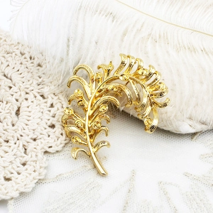 Elegant gold feather brooch with circular hollow design on white lace backdrop