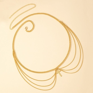 Layered gold punk body chain featuring cross pendant with shiny stones on beige surface