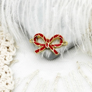 Macro shot of 18k gold plated red enamel bow pendant connector on grey stone