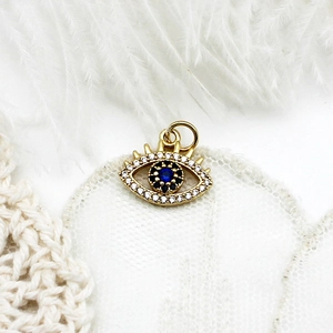 Detailed close-up of 18K gold evil eye charm with micro-pave crystals on white lace