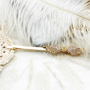 Détail d'une barrette ailes d'ange dorées avec strass blancs sur fond de plumes blanches