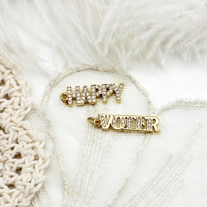 Vue macro des pendentifs HAPPY et VOTER plaqués or 18 carats sur de la dentelle